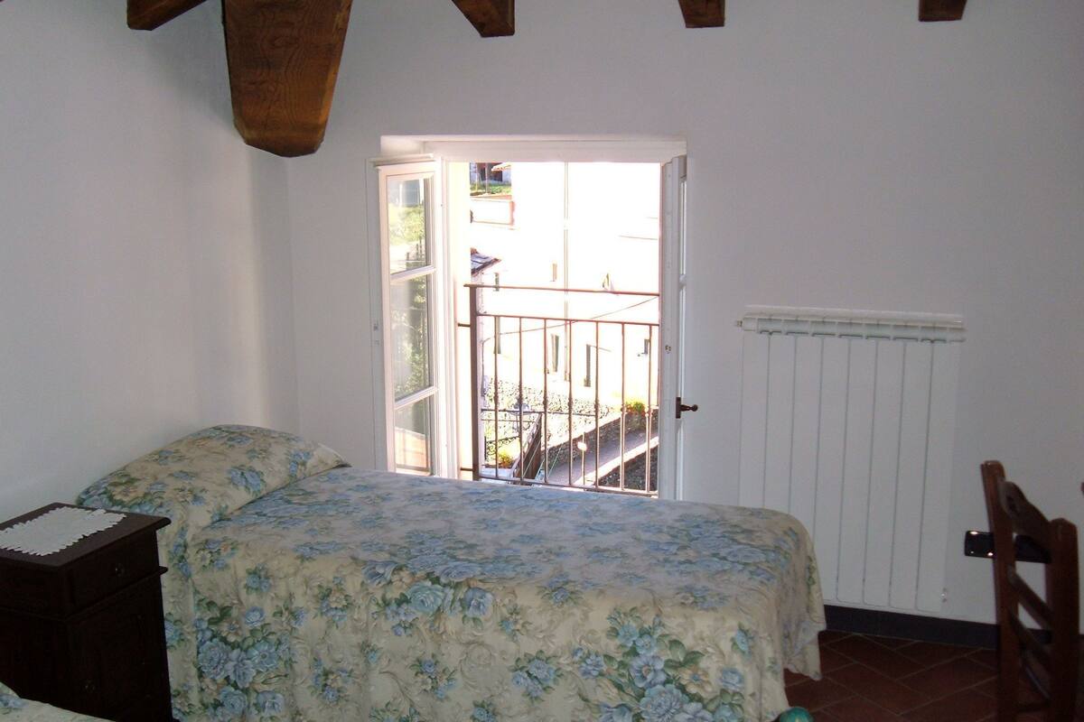 Une chambre à coucher comprenant un lit, une table de chevet, un radiateur et une porte donnant sur un balcon extérieur.