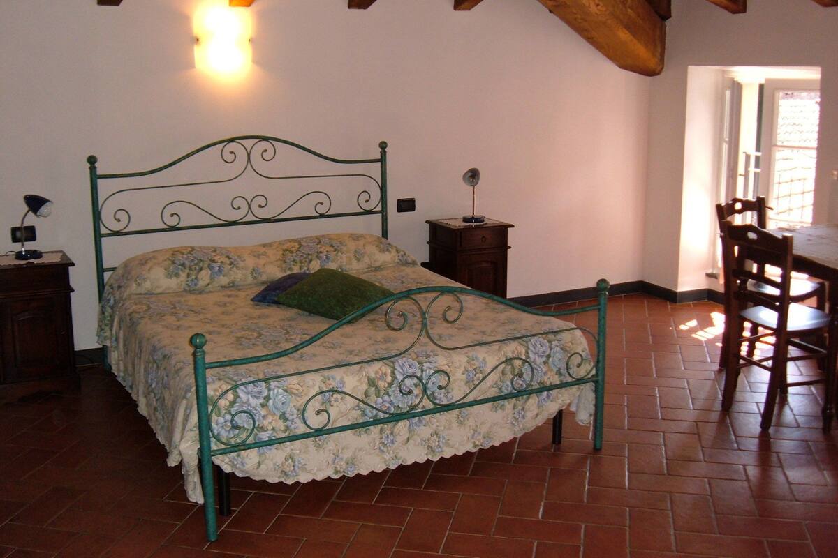 Une chambre avec un lit en métal, une table de chevet en bois, une chaise et un sol carrelé.