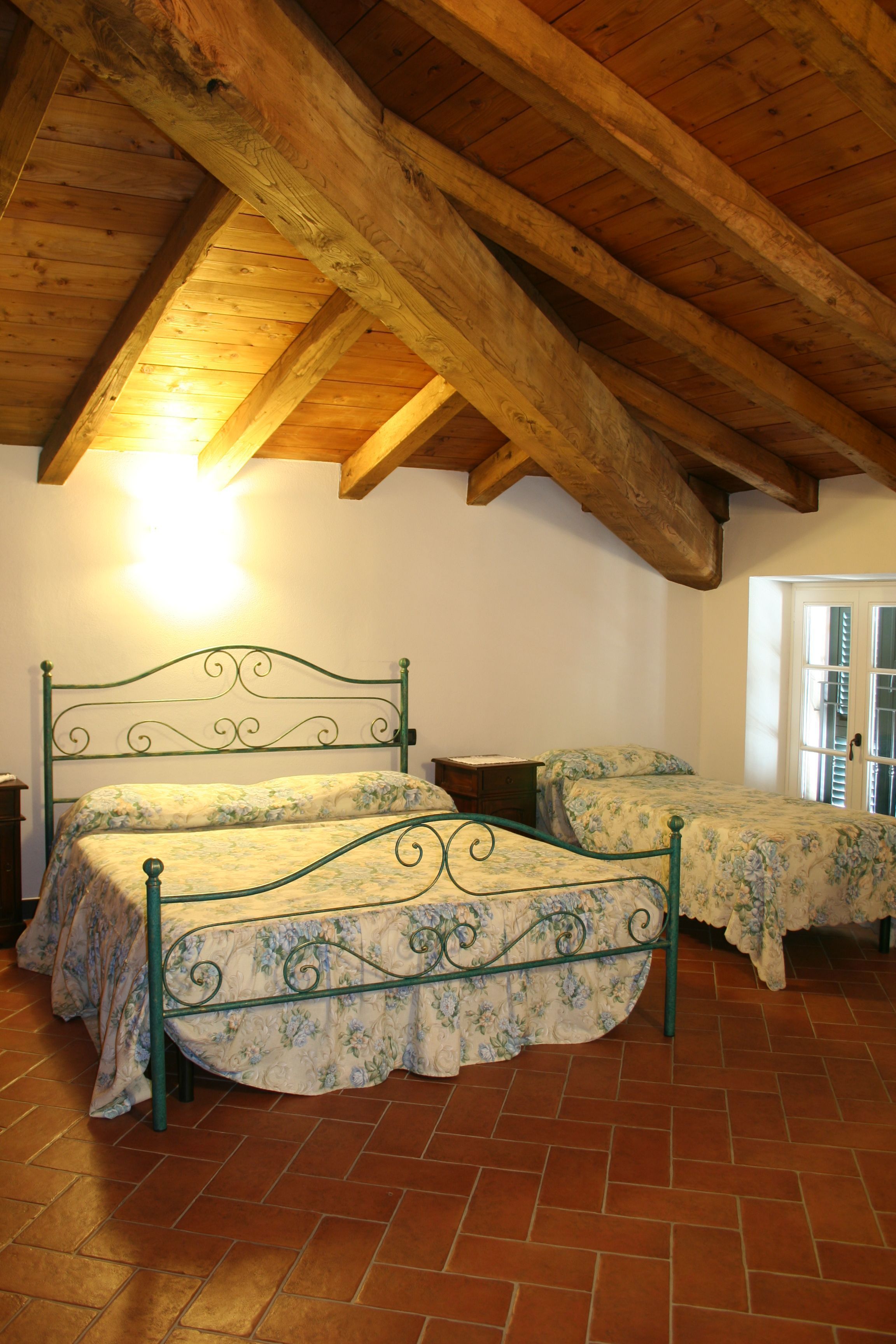 A bedroom with two beds, wooden beams on the ceiling, and a tiled floor.