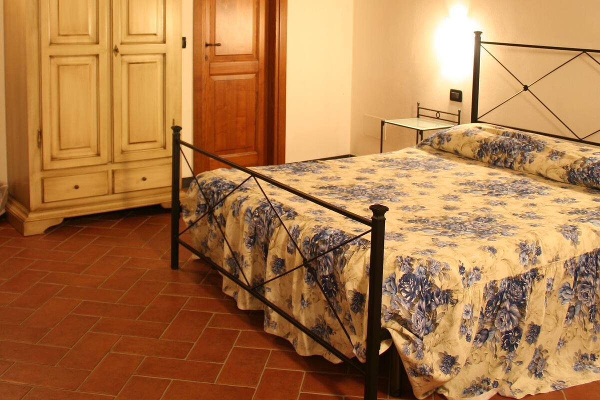 Une chambre avec un plafond en bois, un lit recouvert d’une couvre-lit à motifs floraux, une armoire et une table de chevet.