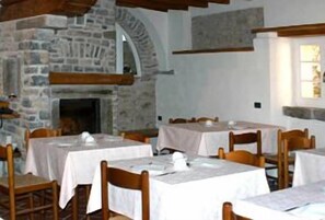 Comedor con paredes de piedra, vigas de madera y mesas dispuestas para comer.