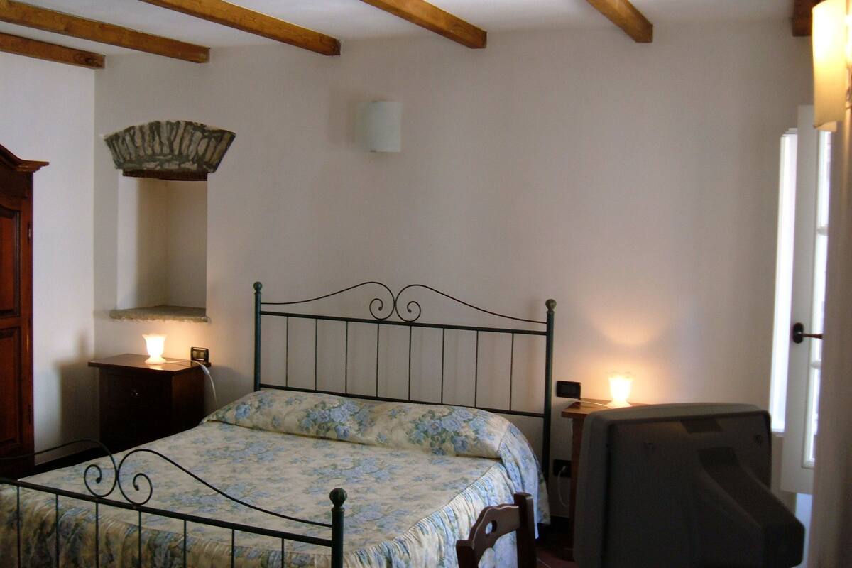 Une chambre à coucher avec un lit, des poutres en bois, une table de chevet, une lampe et une chaise.