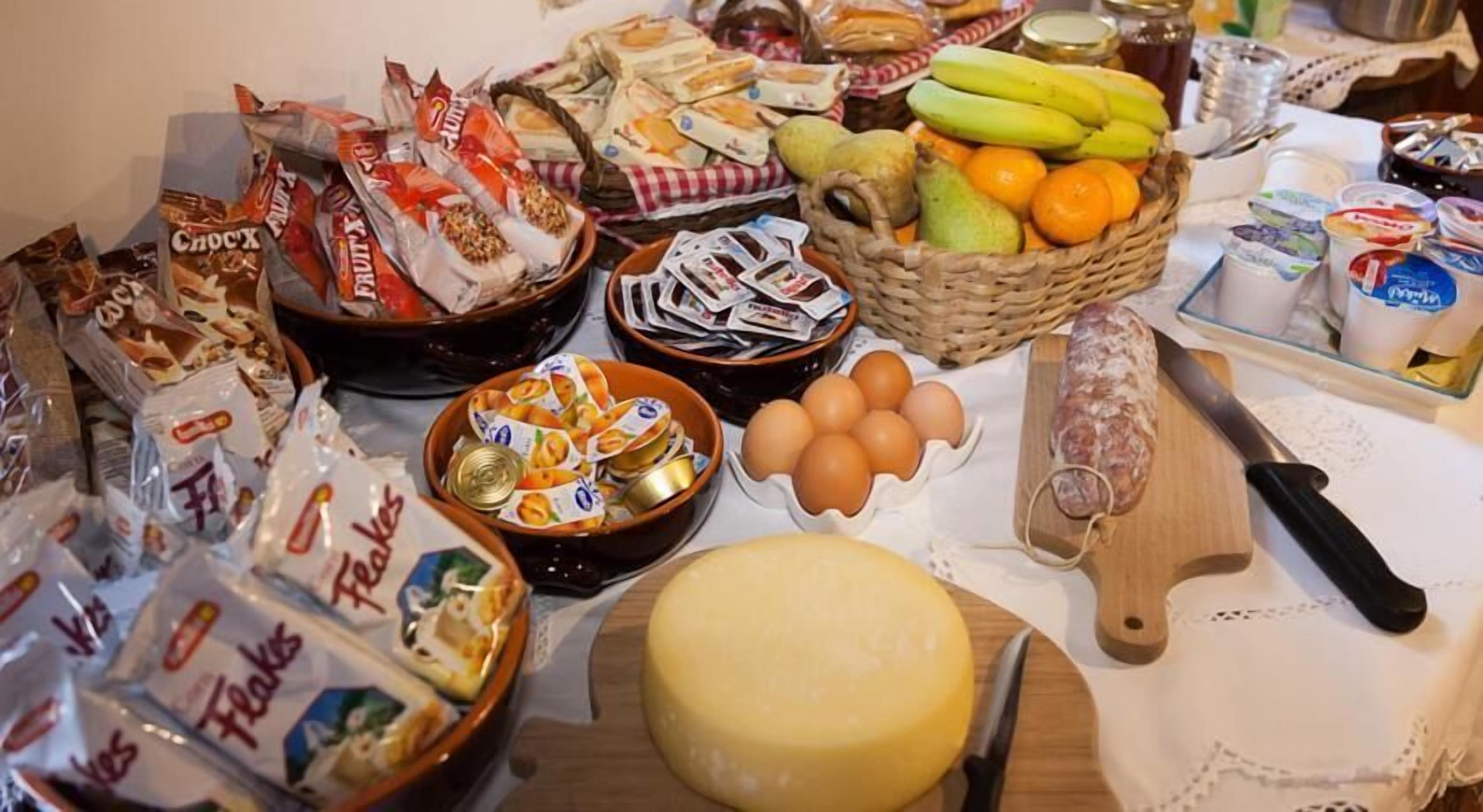 Una mesa con diversos alimentos, entre ellos queso, huevos, frutas y aperitivos envasados.
