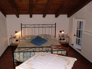 Un dormitorio con una cama, dos mesitas de noche, una silla, una puerta y una ventana.