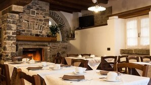 Un comedor con paredes de piedra, chimenea y mesas dispuestas para una comida.