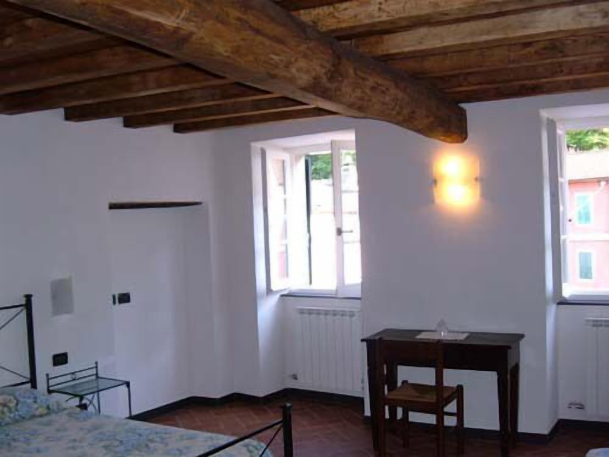 A room with a bed, a table, and a chair. There are windows with curtains and a radiator.