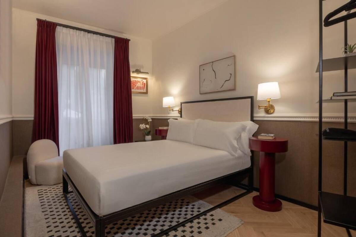 Une chambre d’hôtel avec un lit, une chaise, une table de chevet, une lampe et une horloge murale.