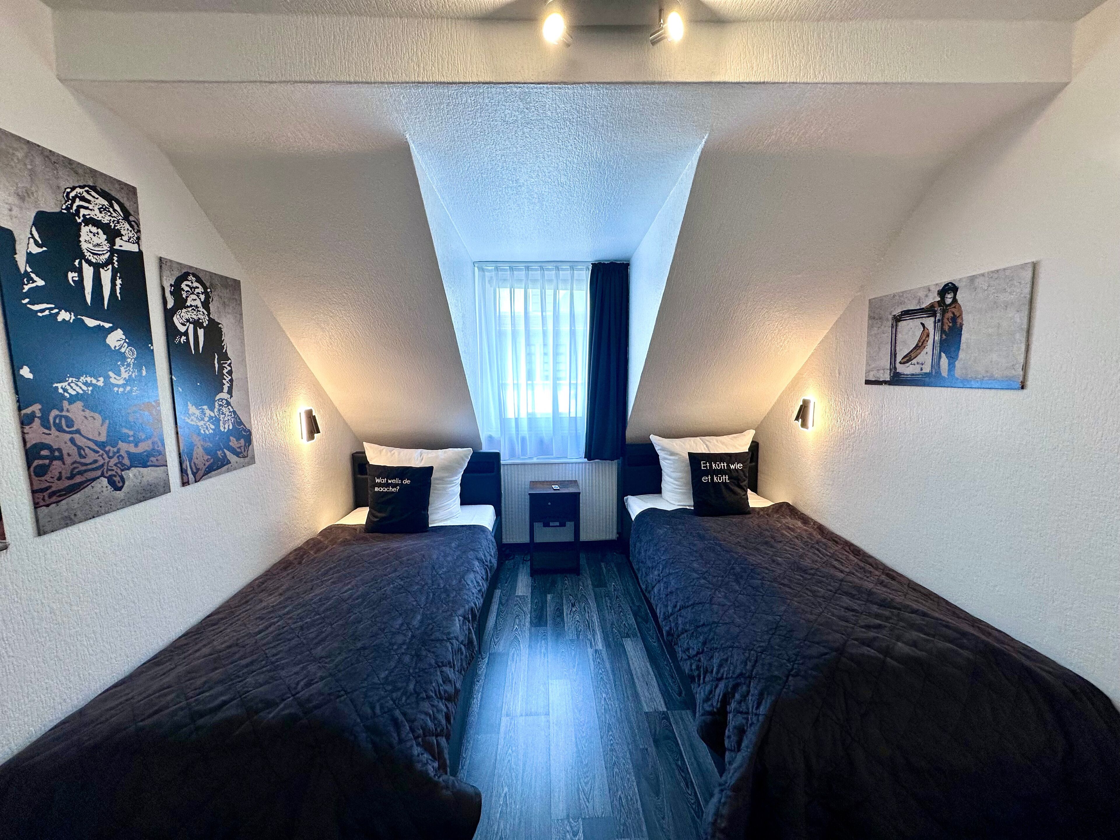 A bedroom with two beds, a window with curtains, and artwork on the walls.