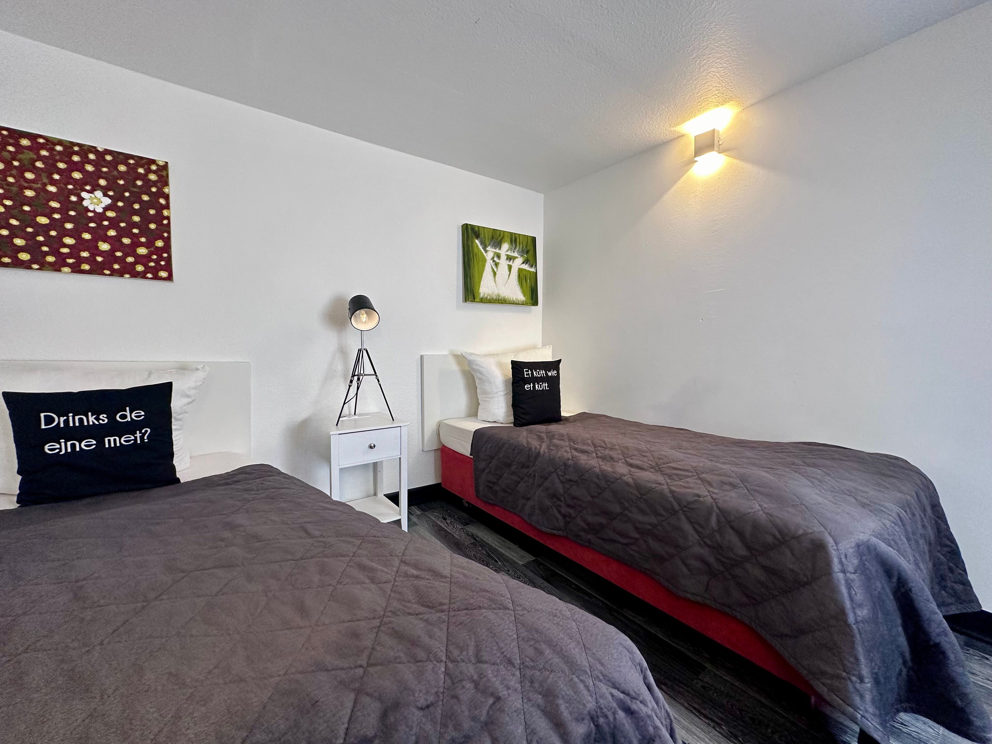Habitació d'hotel amb dos llits, una tauleta de nit, una làmpada i una obra d'art a la paret.