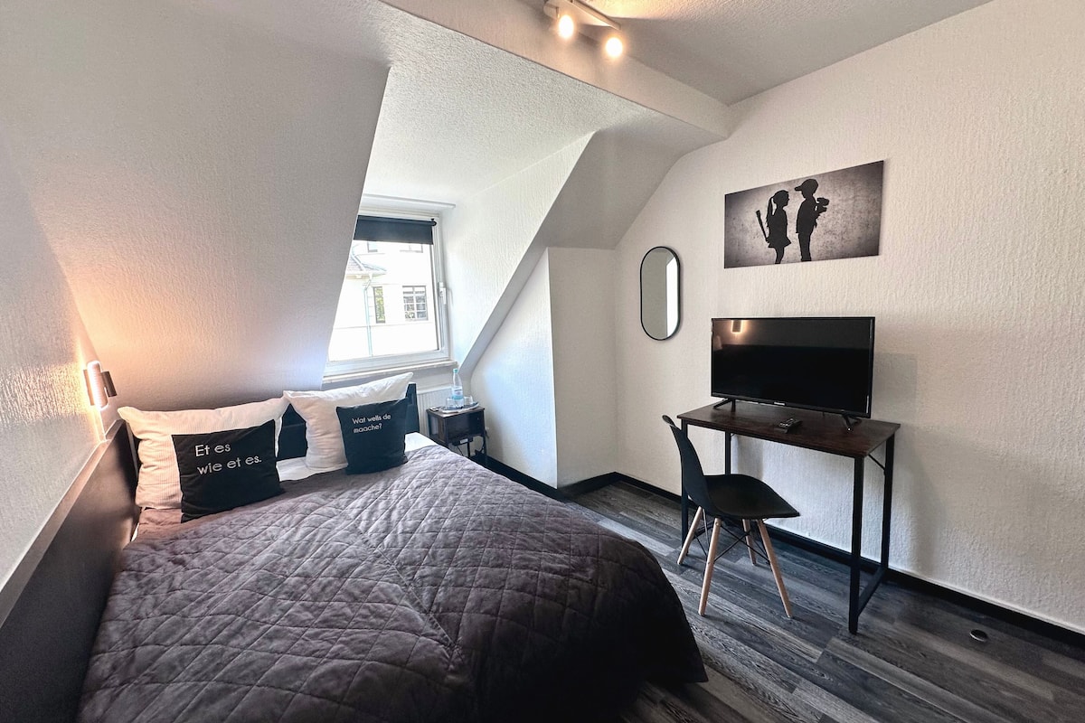 A modern bedroom with a bed, a desk, and a TV.