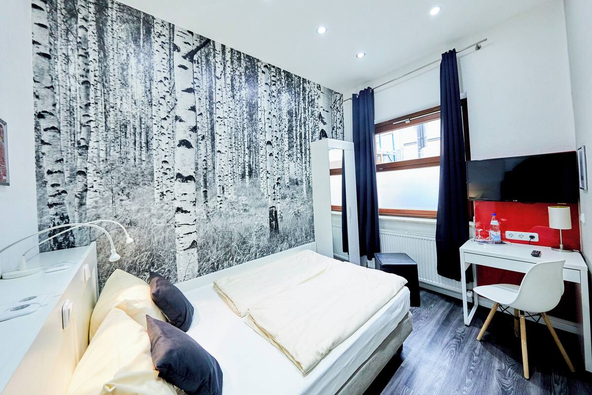 A hotel room with a bed, a desk, a chair, a TV, and a window with curtains.