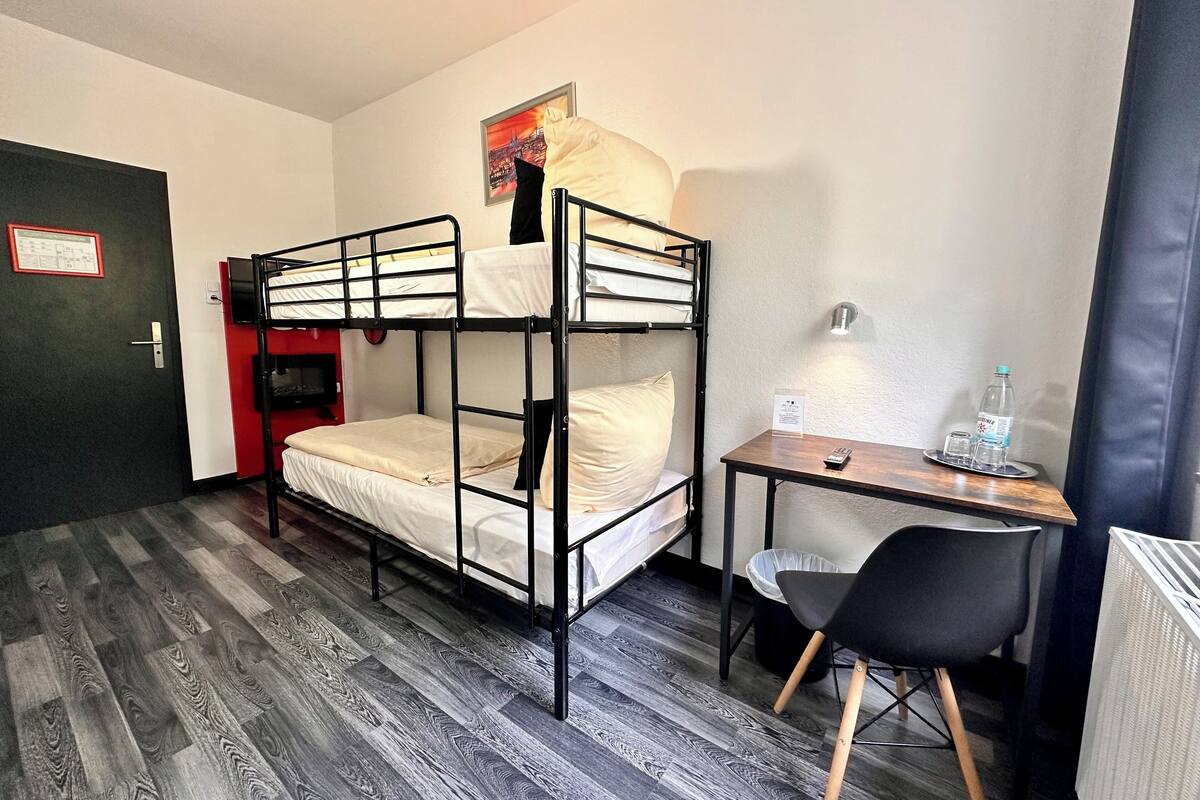 A bunk room with a desk and chair, a trash bin, and a water bottle on the table.