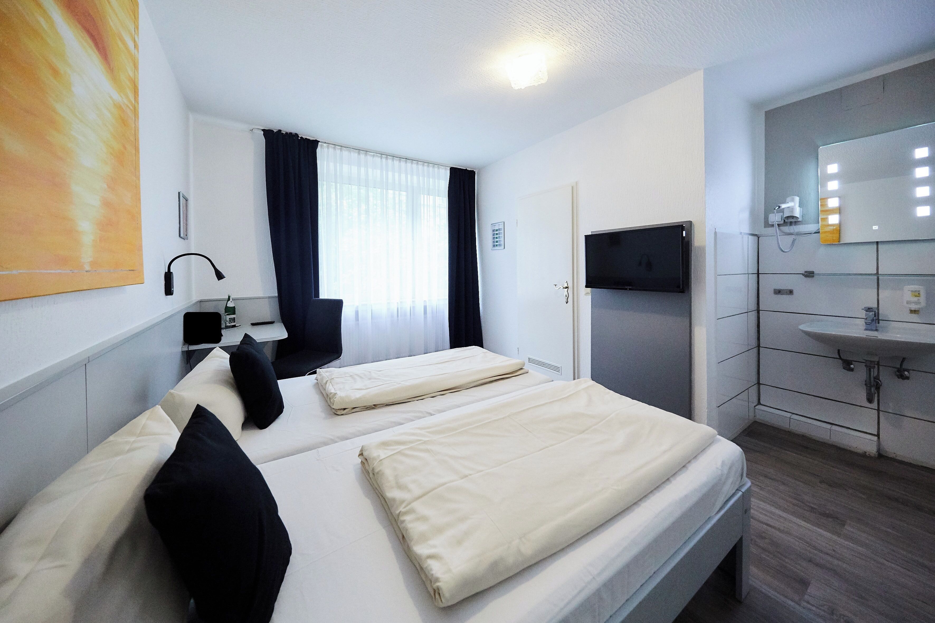 Hotellihuone, jossa on kaksi sänkyä, kylpyhuone, jossa on pesuallas ja peili, sekä televisio.