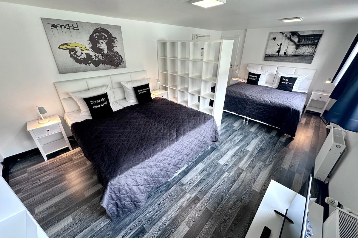 A modern bedroom with two beds, a white wardrobe, and a large artwork on the wall.