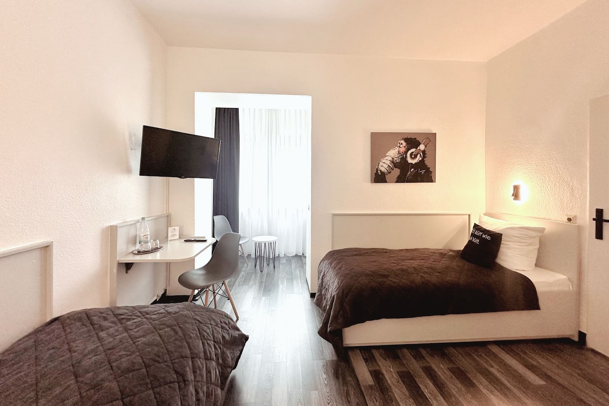A hotel room with two beds, a desk, a chair, a TV, and a painting on the wall.