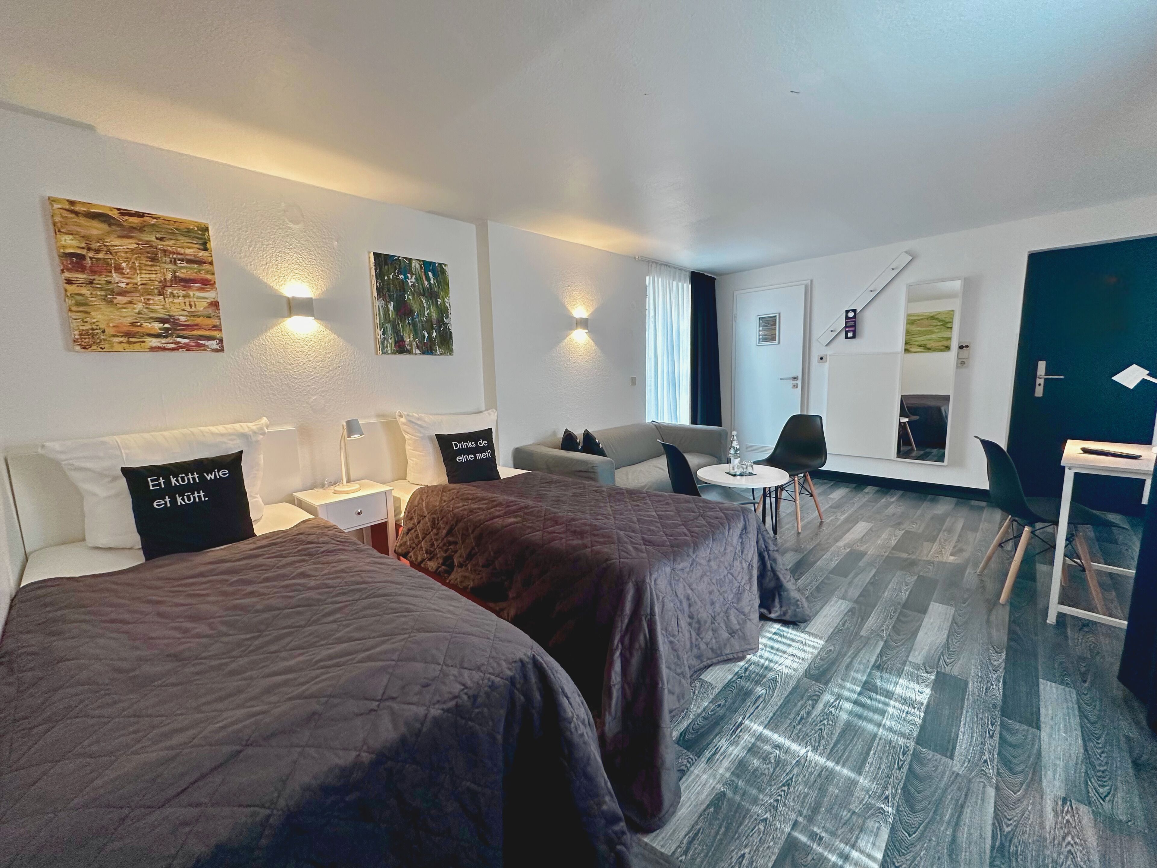 Een hotelkamer met twee bedden, een slaapbank, een kleine tafel en een stoel. Er zijn wandlampen en kunstwerken aan de muren.