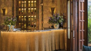 A bar area with a wooden counter, two flower vases, and a large arched window with bottles behind it. - Posada La Sacristía (Tarifa)