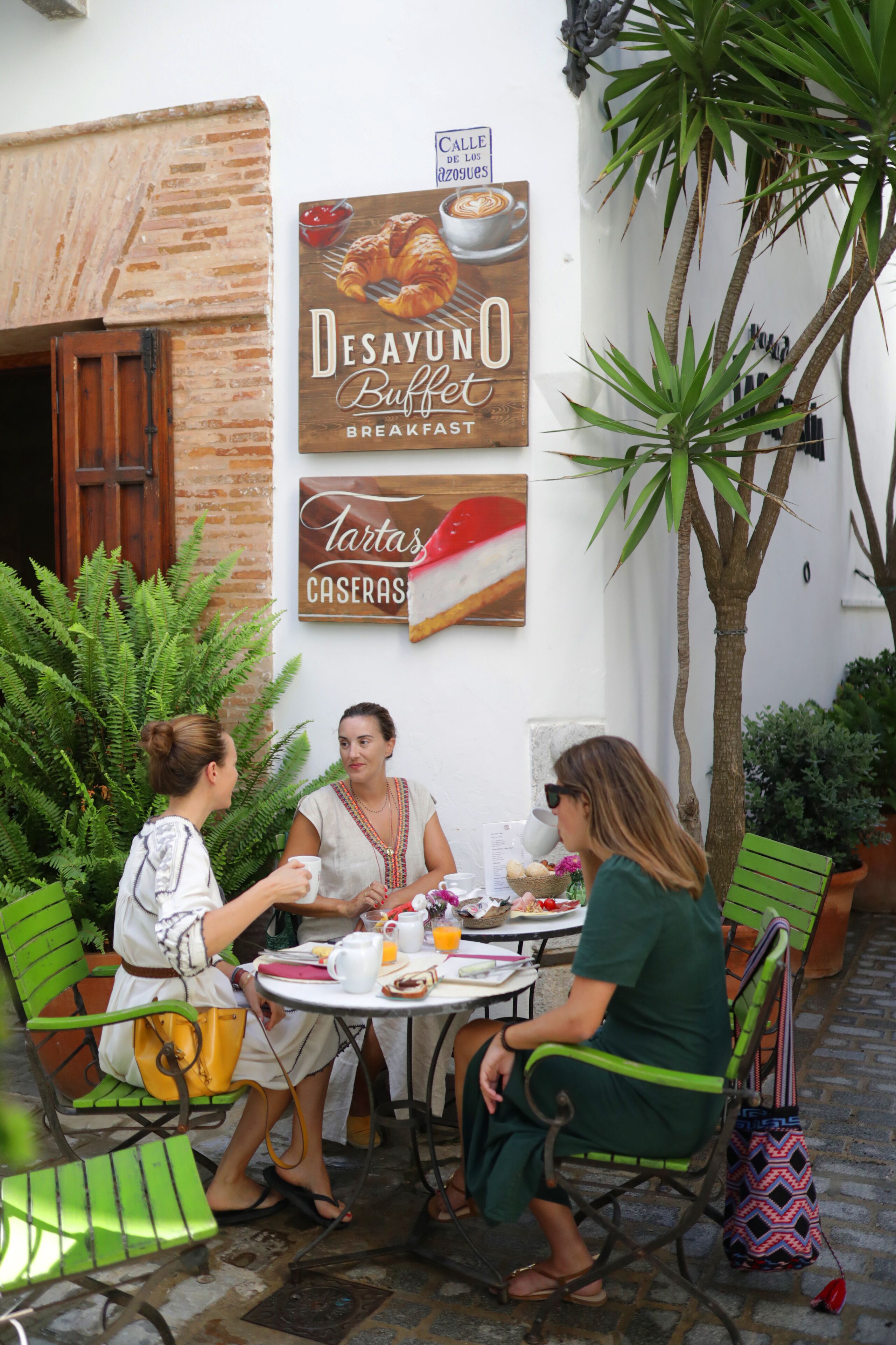 Tres personas sentadas en una mesa al aire libre con un letrero que anuncia el desayuno.