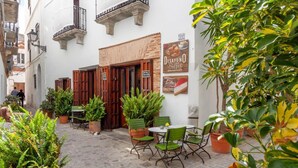 An outdoor café area with wooden shutters, potted plants, and outdoor seating. - Posada La Sacristía (Tarifa)