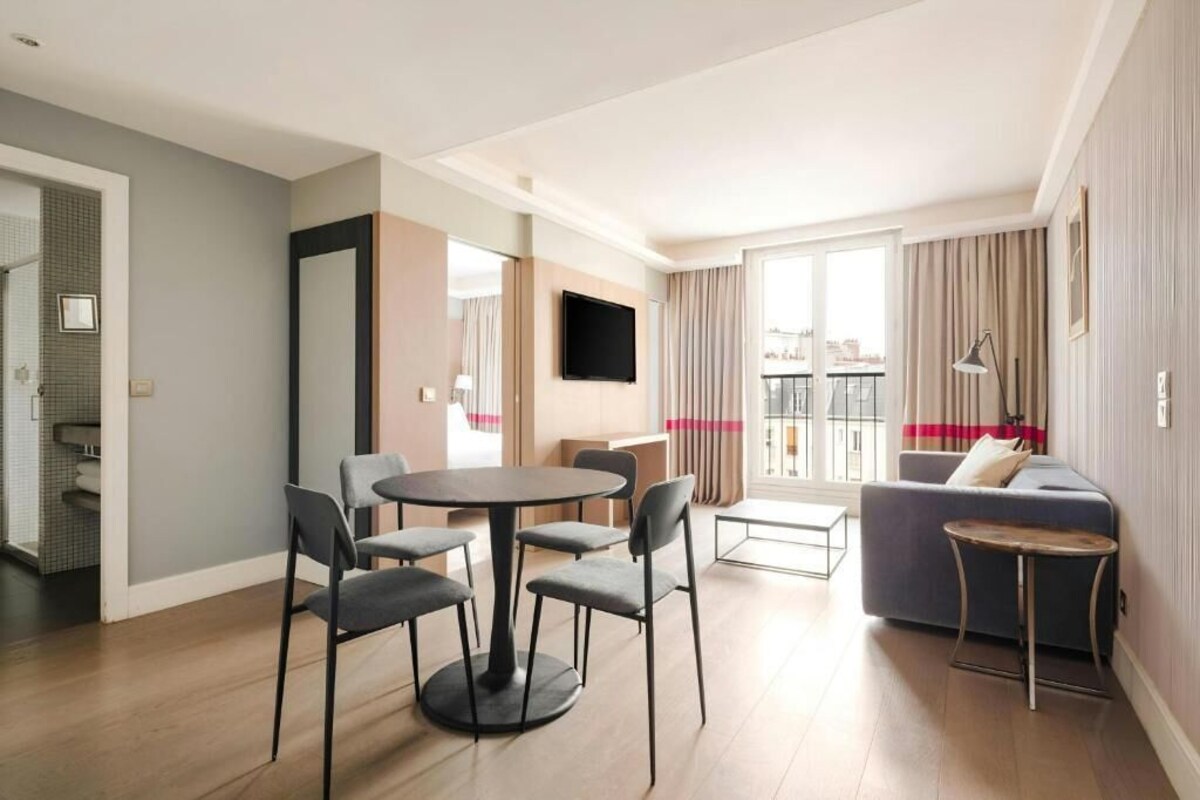 A modern living room with a round dining table, grey chairs, a sofa, and a TV mounted on the wall.