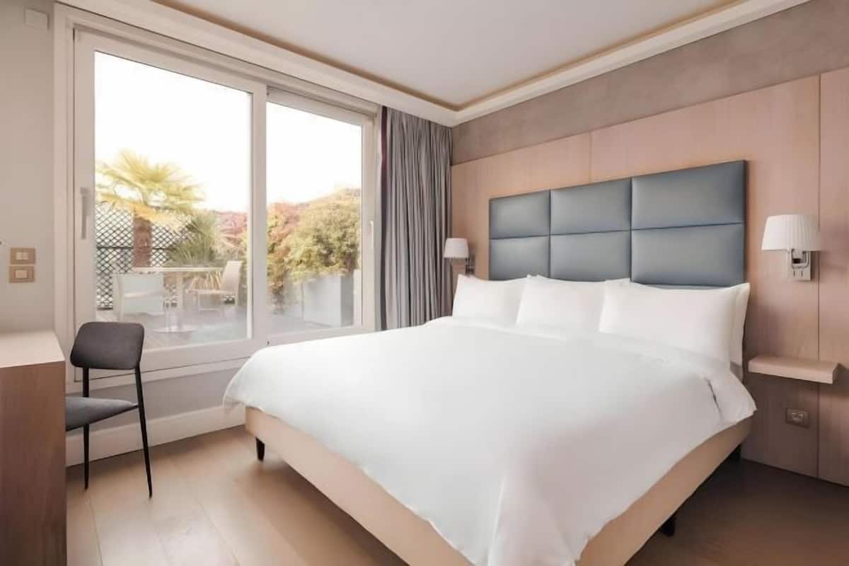 A hotel room with a large bed, a chair, a desk, and a view of the outdoors.