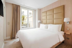 A hotel room with a large bed, a window with curtains, a wall-mounted TV, and a bedside table with a lamp. - L’Edmond Hotel Parc Monceau (Paris)