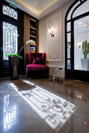 A lobby with a red armchair, a large potted plant, and a decorative mirror. - L’Edmond Hotel Parc Monceau (Paris)