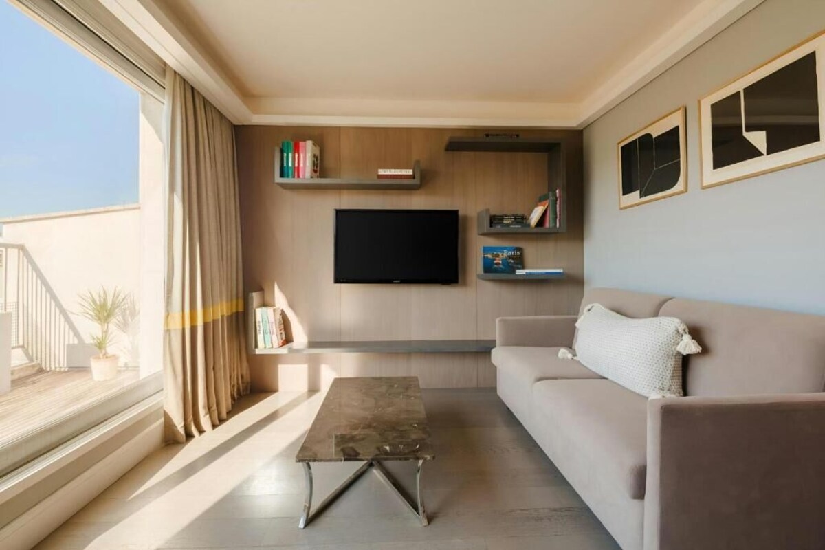A modern living room with a sofa, a coffee table, a TV mounted on the wall, and a bookshelf.