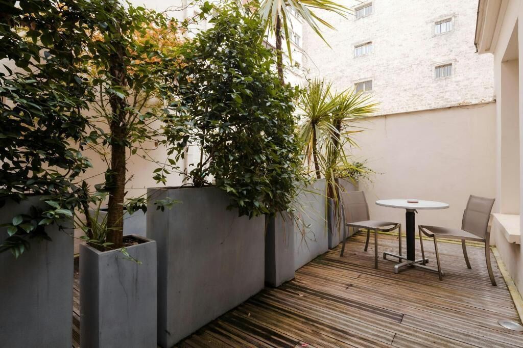 A small outdoor patio area with a round table and two chairs, surrounded by potted plants and a wooden deck.