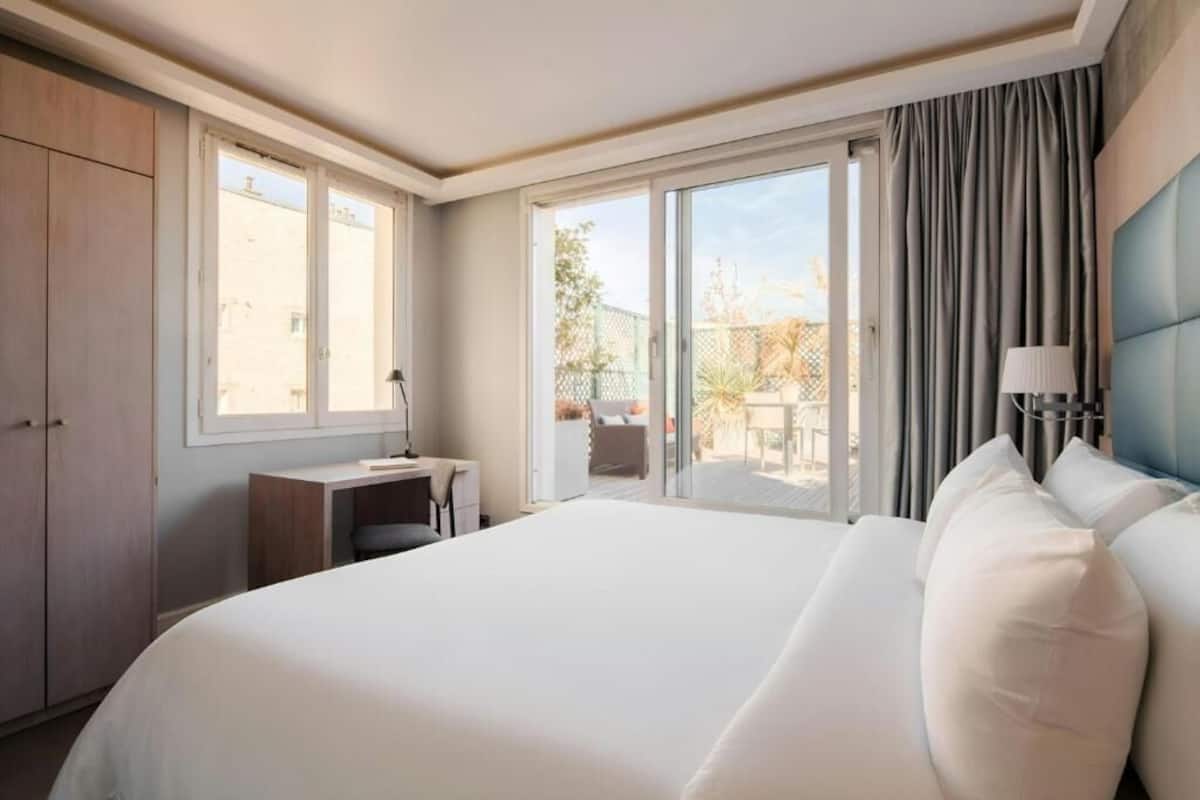 A hotel room with a large bed, a desk, and a view of the outside.