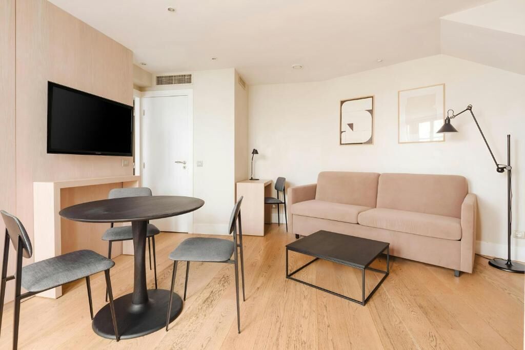 Un salon moderne avec une table ronde, deux canapés et un téléviseur à écran plat fixé au mur.