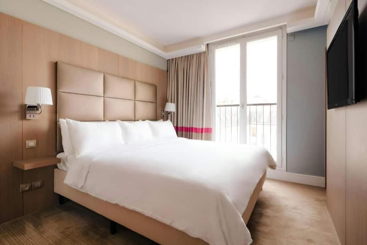 A hotel room with a large bed, a flat-screen TV, a bedside table, and a window with curtains.