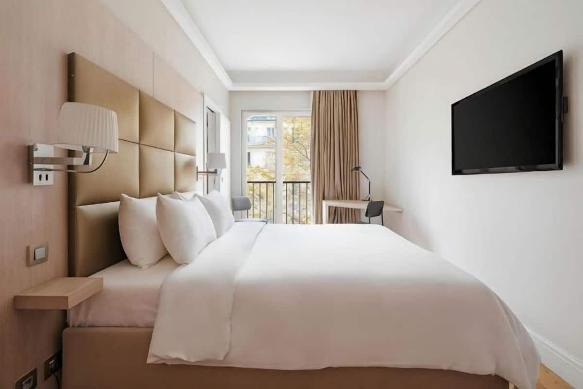 A hotel room with a bed, a TV, a desk, and a balcony.