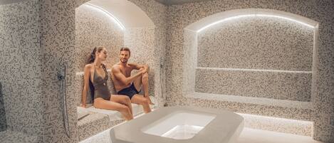 A modern bathroom with mosaic tile walls, a freestanding bathtub, and a bench.