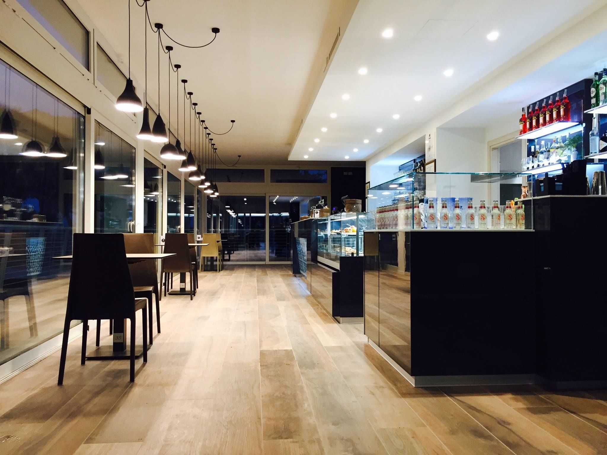 Un interno ristorante moderno con un lungo bancone, lampade a sospensione e una vetrina.