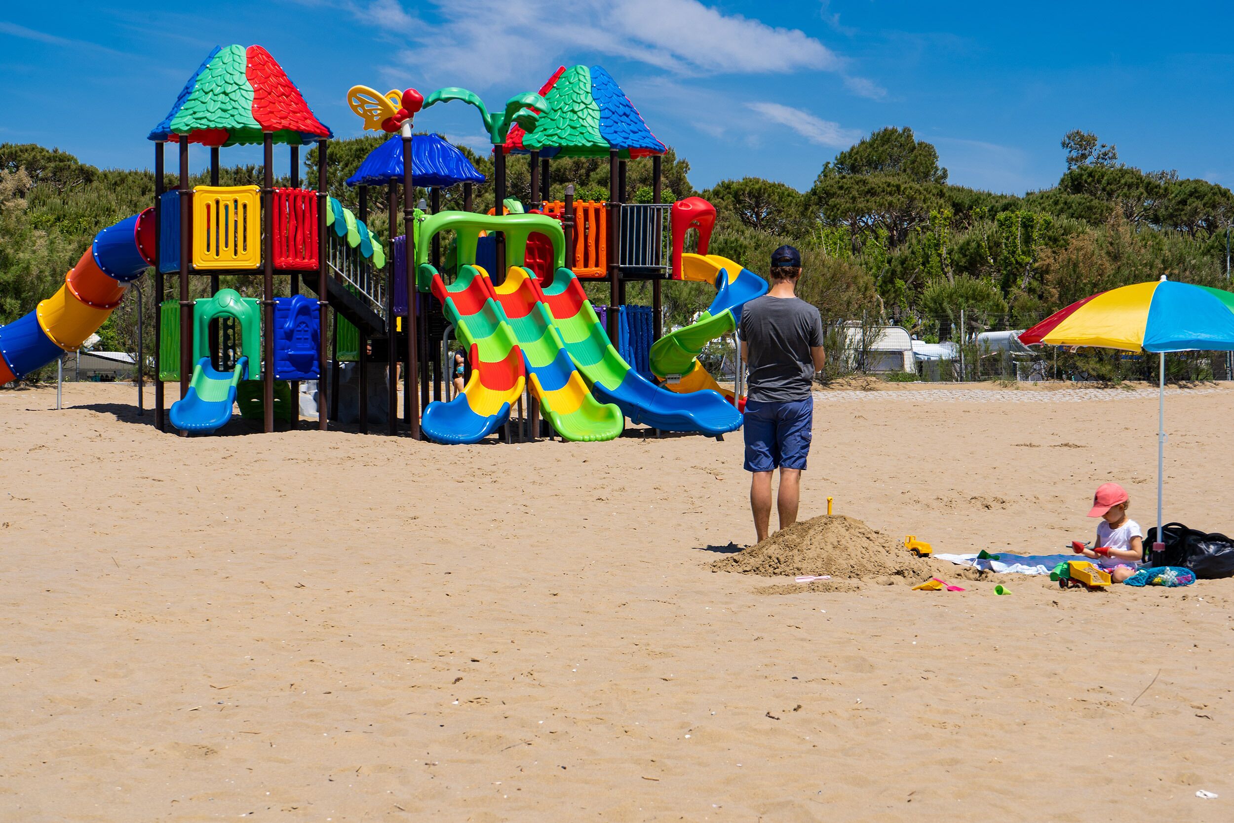 Een strand met een kleurrijke speelconstructie, inclusief glijbanen en klimgebieden.