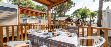 A covered outdoor dining area with a table set for breakfast, surrounded by white plastic chairs.