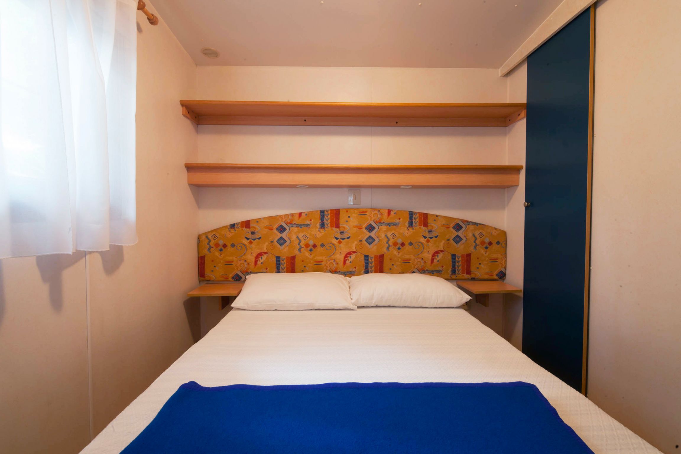 Une chambre avec un lit simple, une tête de lit en bois, une couvre-lit bleue et un oreiller blanc.