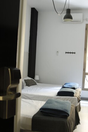 A hotel room with two beds, a hanging lamp, a wall-mounted air conditioner, and a coat rack. - Feel Hostels Soho Malaga (Málaga)