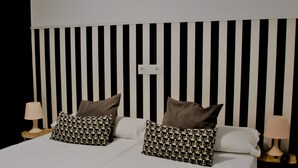 Una cama con cabecera a rayas negras y blancas, dos lámparas de noche y almohadas estampadas.