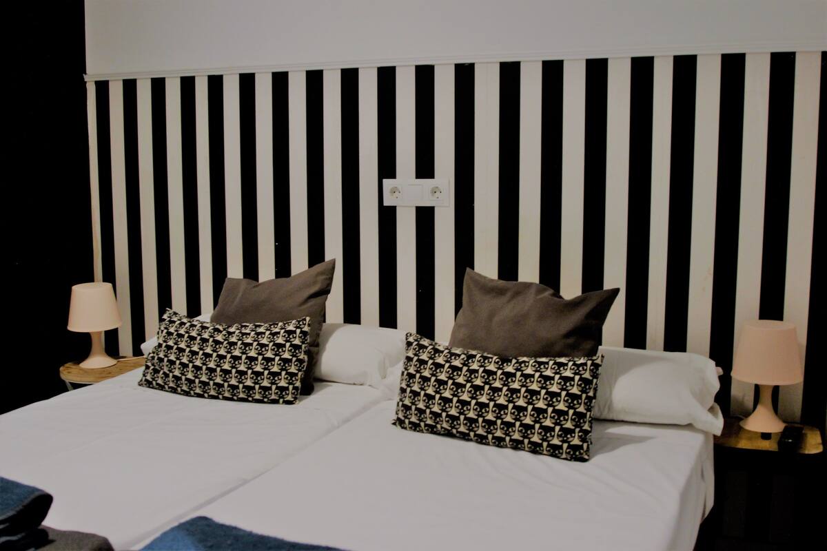 A bed with a black and white striped headboard, two bedside lamps, and patterned pillows.