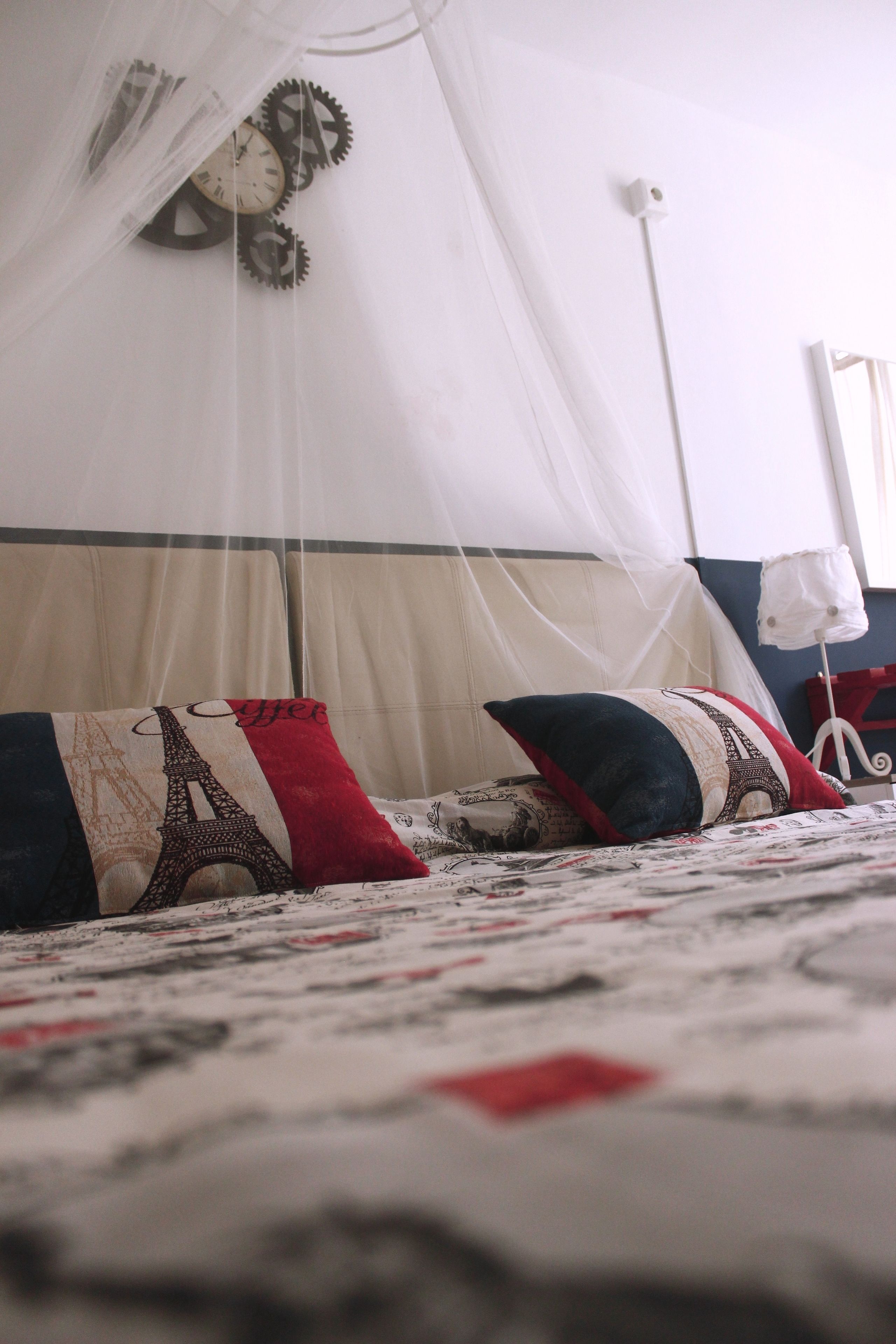 Una cama con una colcha estampada, dosel y almohadones decorativos, incluyendo uno con diseño de la Torre Eiffel.