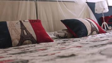 Una cama con una colcha estampada, dosel y almohadones decorativos, incluyendo uno con diseño de la Torre Eiffel.