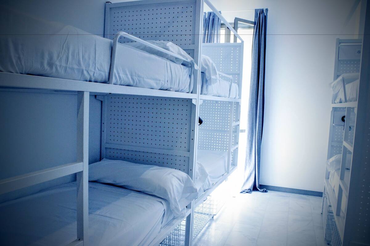 A bunk bed room with a metal frame, white bedding, and a window with curtains.