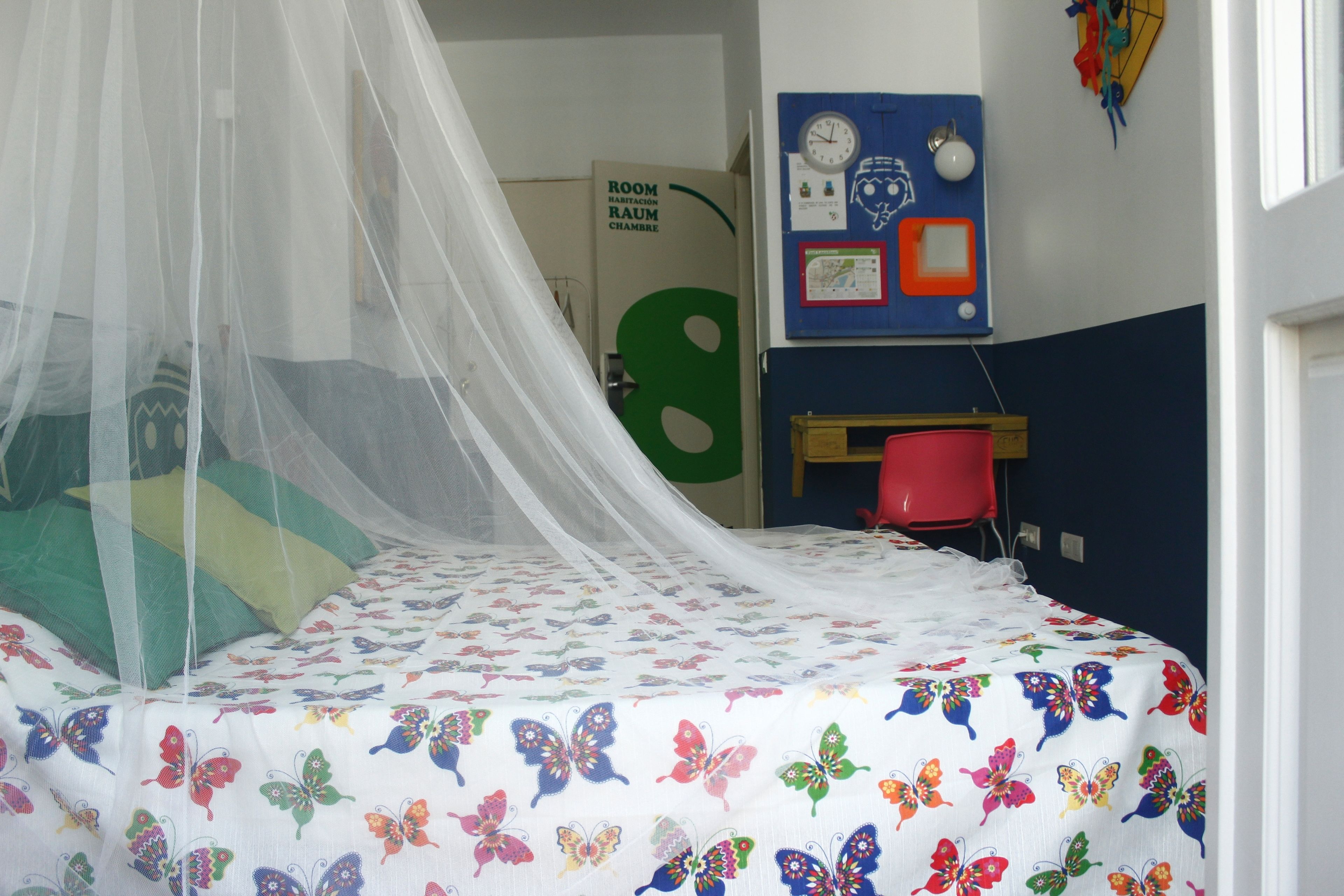 A bed with a mosquito net, colorful butterfly bedding, a desk, and a clock on the wall.