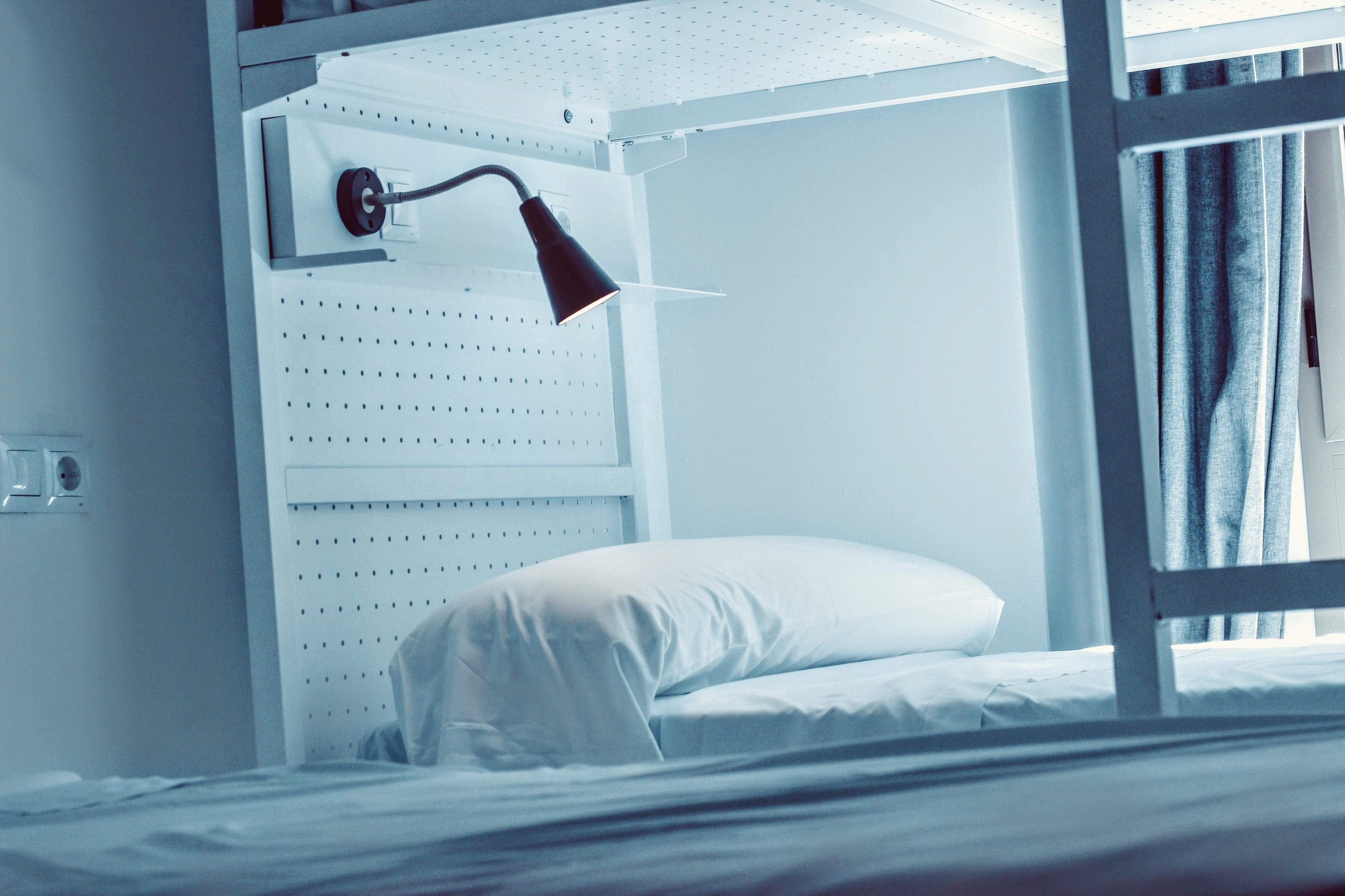 A bunk bed with a white headboard, a red desk lamp, and a white pillow.