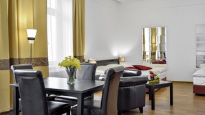 Een moderne hotelkamer met een zithoek, een bed met rode kussens, een nachtkastje met een lamp en een grote spiegel aan de muur.
