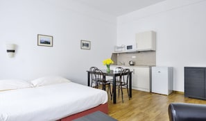 A hotel room with a bed, a small dining table with chairs, a kitchenette, and a compact refrigerator. - Apartments Central Park Marienbad (Marianske Lazne)