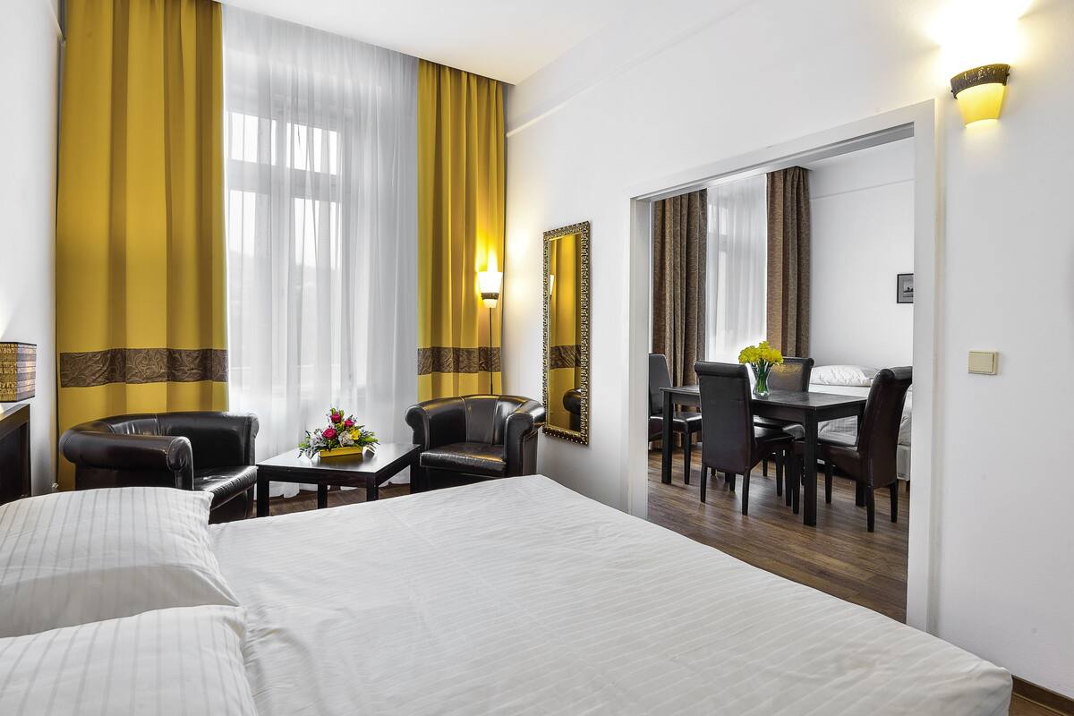 A hotel room with a large bed, a desk with a chair, a mirror, and a view of a dining area.