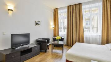 A hotel room with a bed, a TV, a desk with a vase of flowers, and a chair.